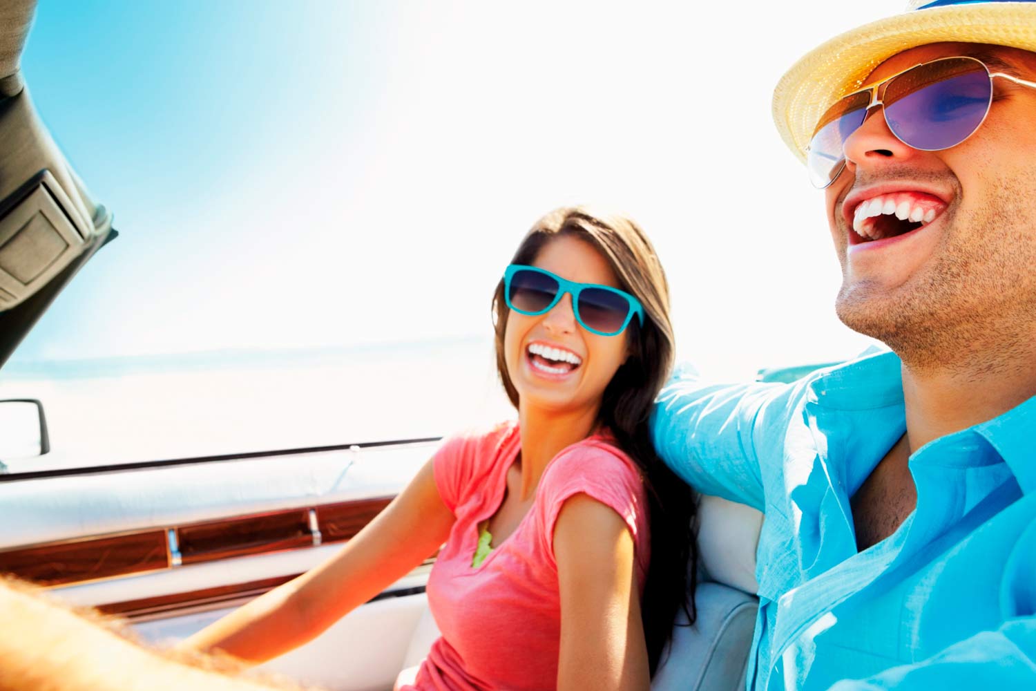 Homem e mulher de óculos de sol e sorridentes, em carro descapotável