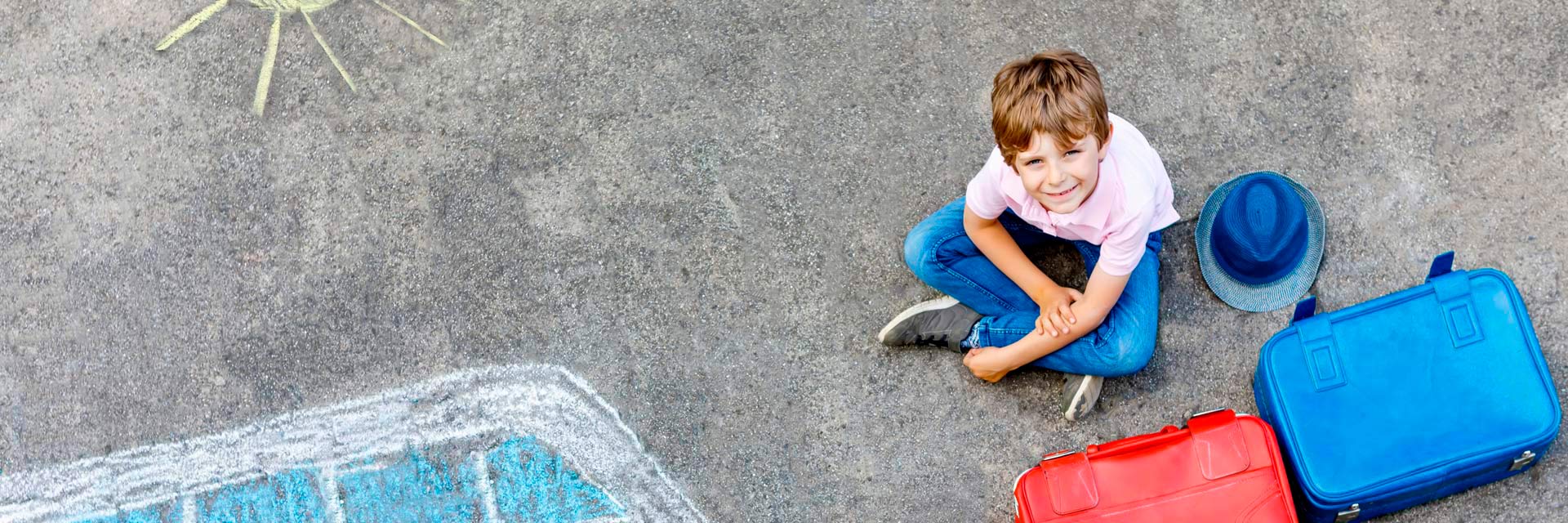 Criança sentada no chão com malas acompanhada de desenho de comboio no chão.