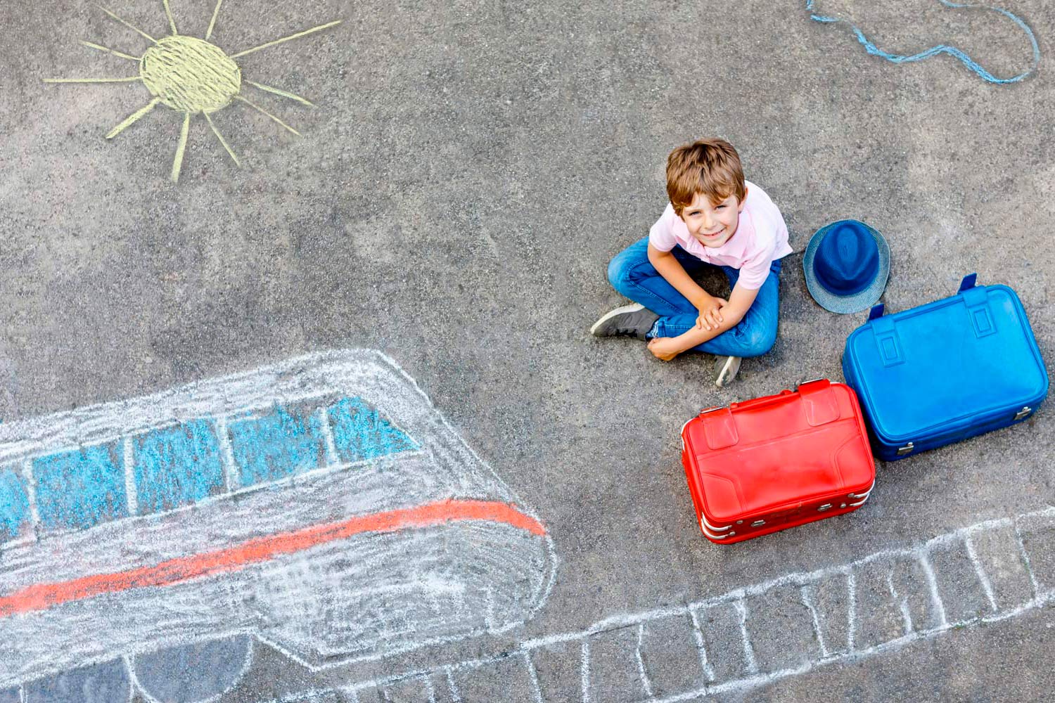 Criança sentada no chão com malas acompanhada de desenho de comboio no chão.