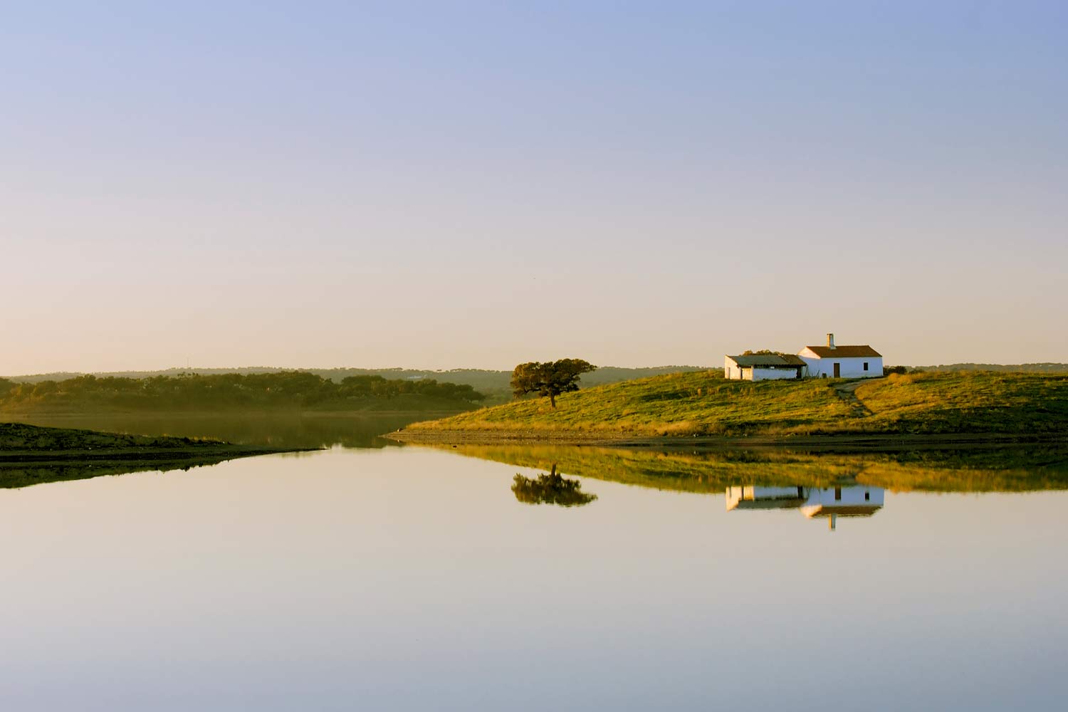 Imagem do campo alentejano com duas casas e uma arvore refletidas num lago