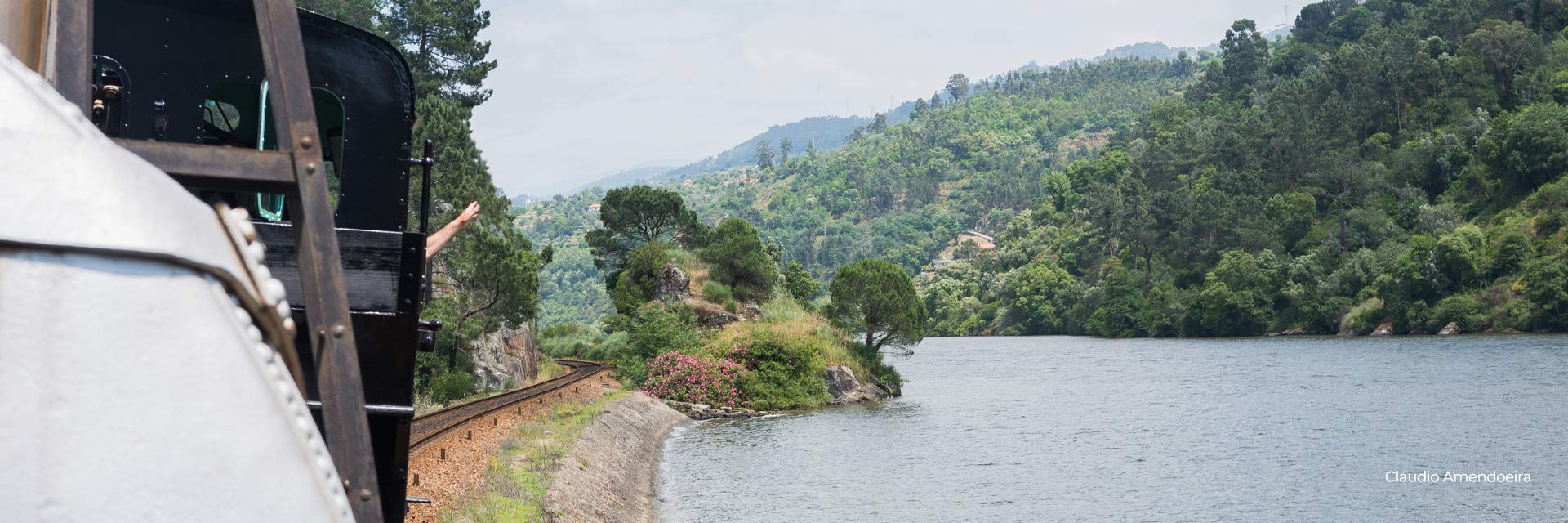 View from a train window with the steam locomotive ahead, the train line very close to the banks of the Douro River.
