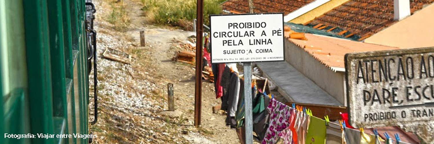 A sign warning of passing trains, alongside the track between a house and the train.
