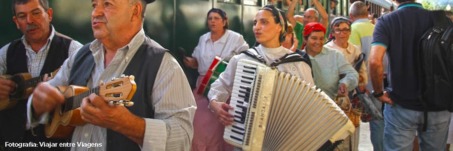 Musicians playing a small guitar, accordion and drum, along with other members of the folk dance troupe.
