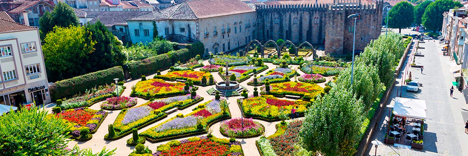 Jardim de Santa Bárbara com flores em canteiros de várias formas e uma fonte no centro e algumas árvores em volta.