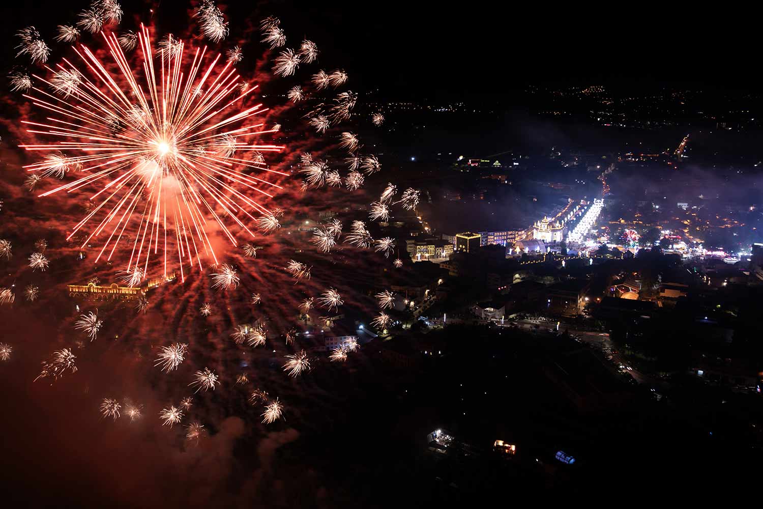A night-time aerial view of the town of Barcelos, lit up and with fireworks from the festival.