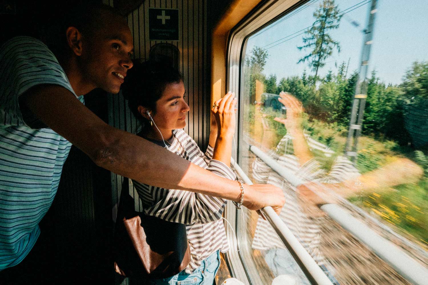 Casal jovem a sorrir e a fotografar pela janela do comboio.
