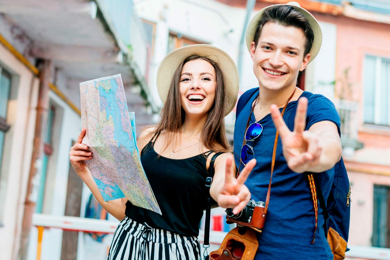 Casal jovem sorridente, ele com câmera fotográfica pendurada ao pescoço e ela com mapa na mão.