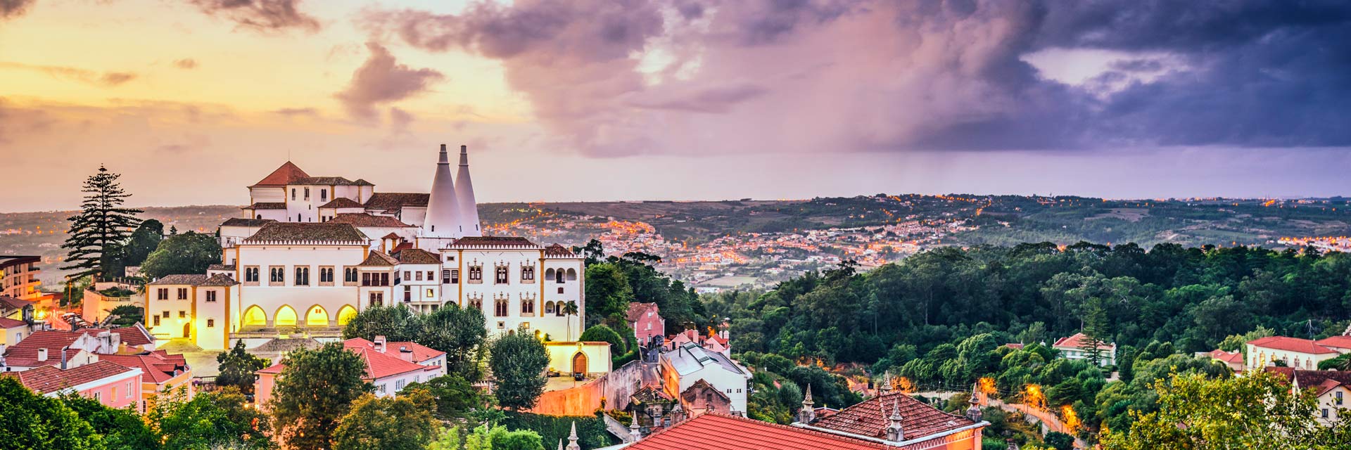 View of the National Palace of Sintra, some rooftops and green areas, in the late afternoon light.