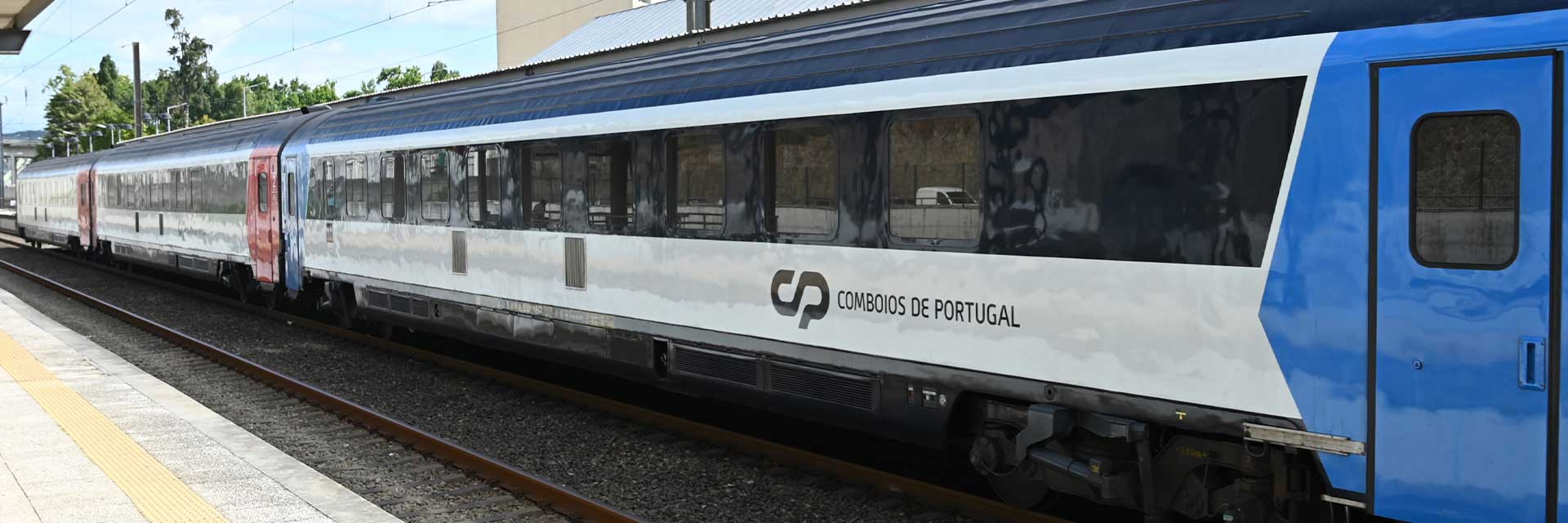 Carruagens Arco em tons de branco, vermelho e azul, paradas na plataforma da estação.