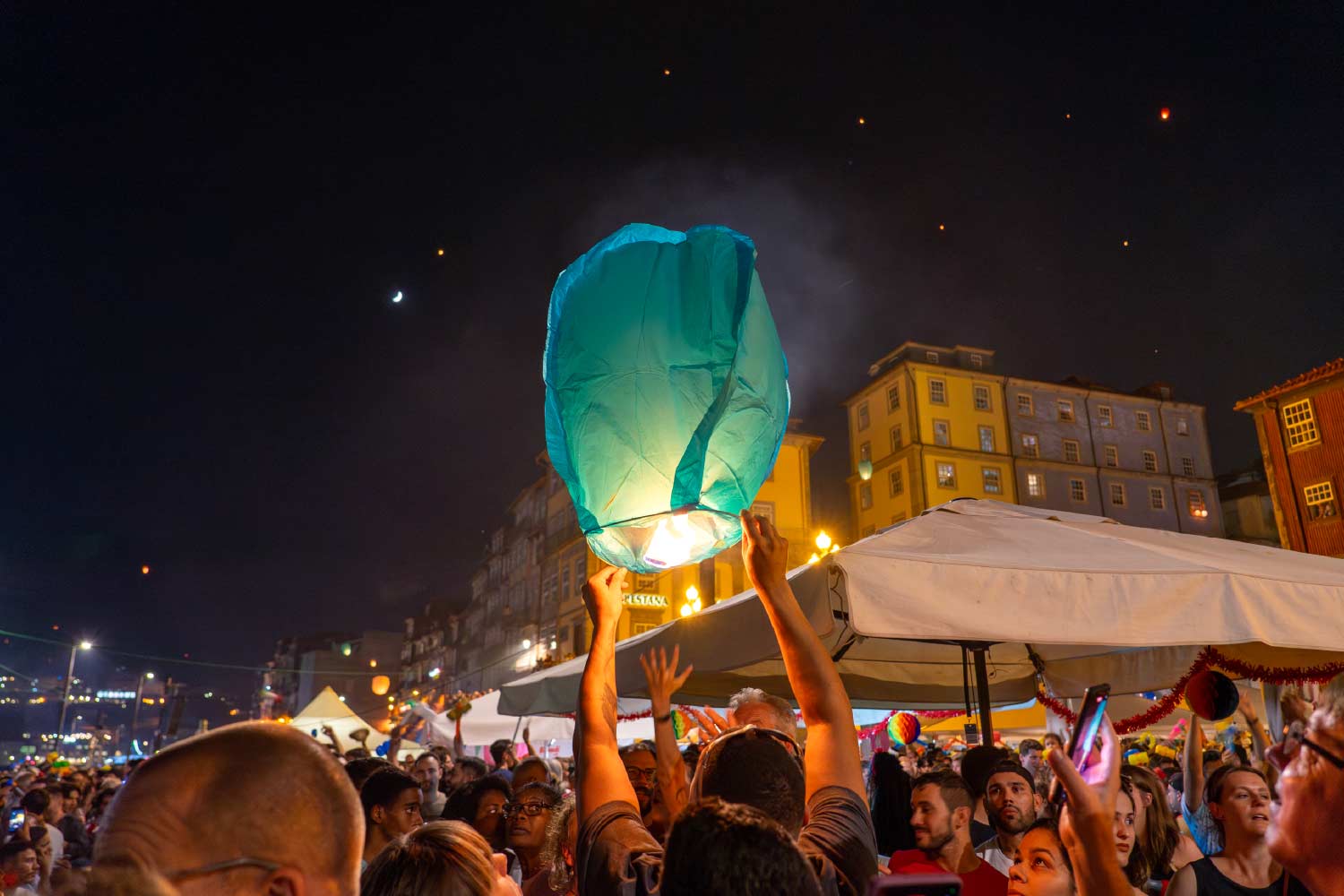 Multidão na Ribeira do Porto em noite de  São João, com uma pessoa a segurar um balão aceso.