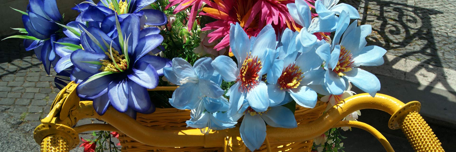 Plano de cesto de bicicleta amarelo, coberto de flores de diferentes cores, decoração do comércio local.