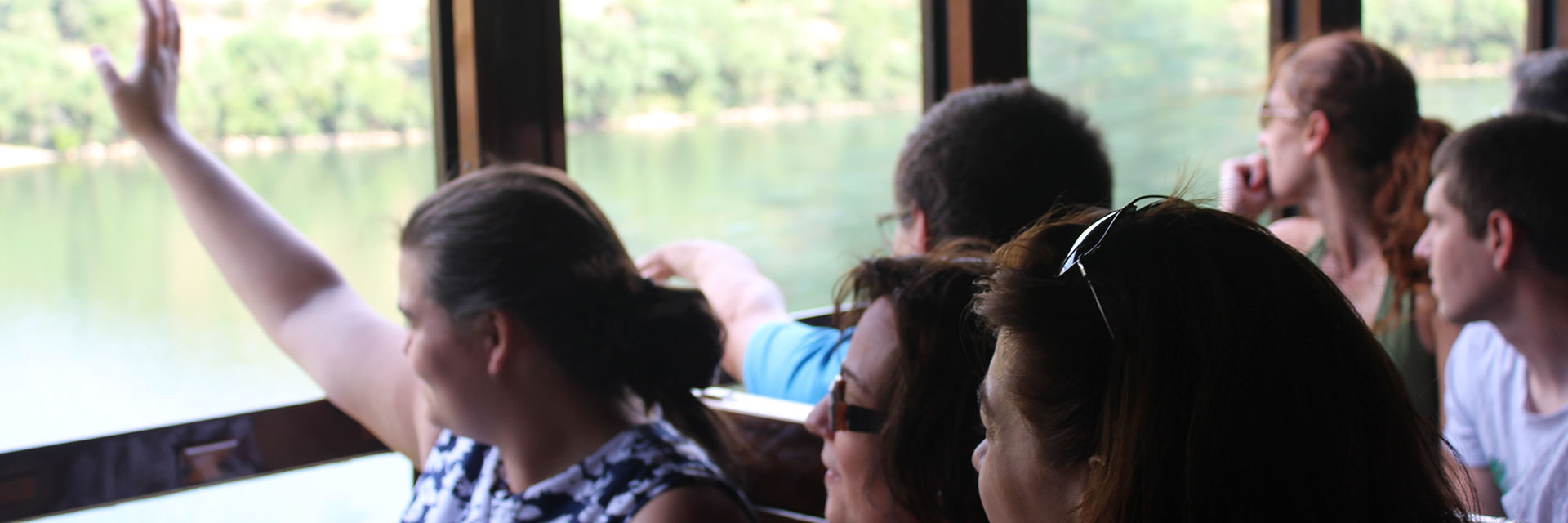 People sitting on the train waving to boats passing on the river.