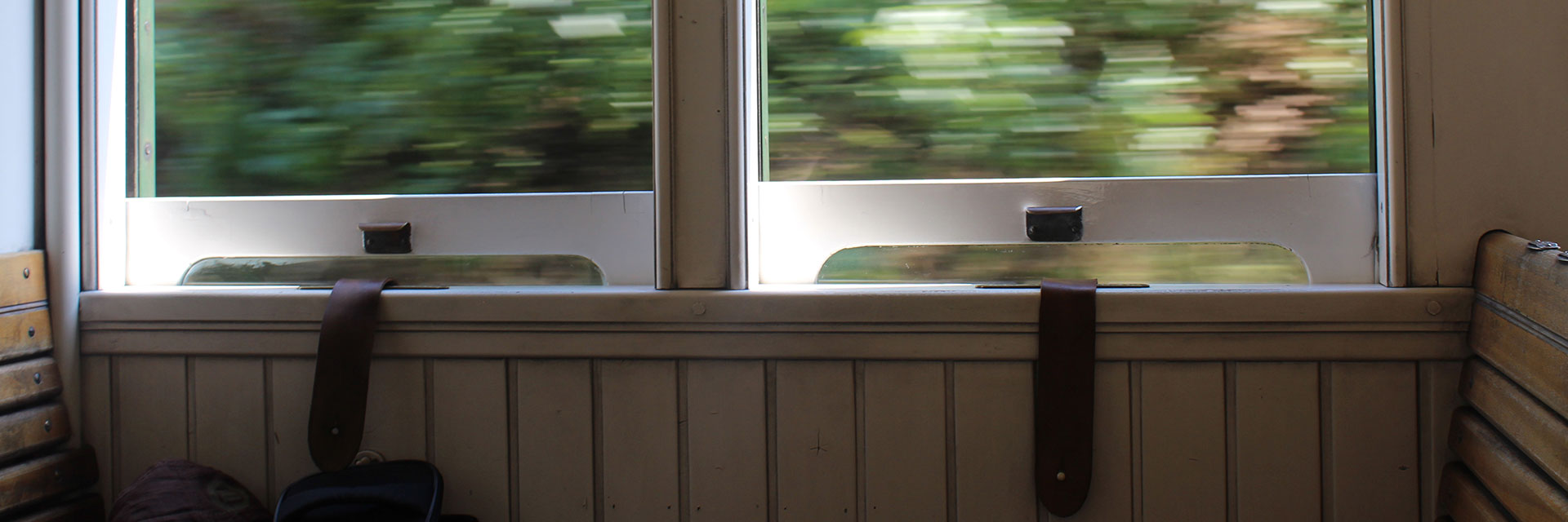 Interior of a historic wooden carriage, with the windows open and the latches on leather straps, and the wooden seat backs.