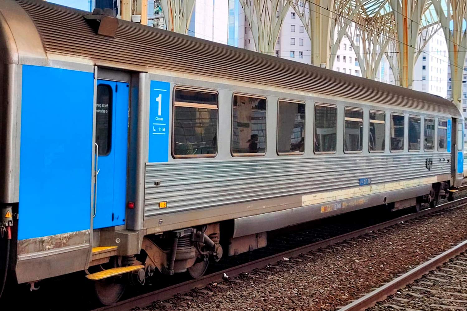 Carruagem Corail de 1ª classe cor azul e cinzento parada na estação.