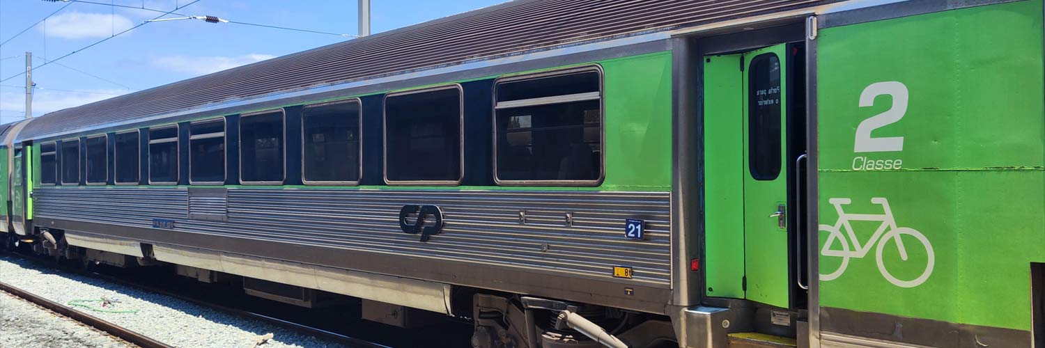 Carruagem Corail de 2ª classe cor verde e cinzento parada numa das linhas da estação.