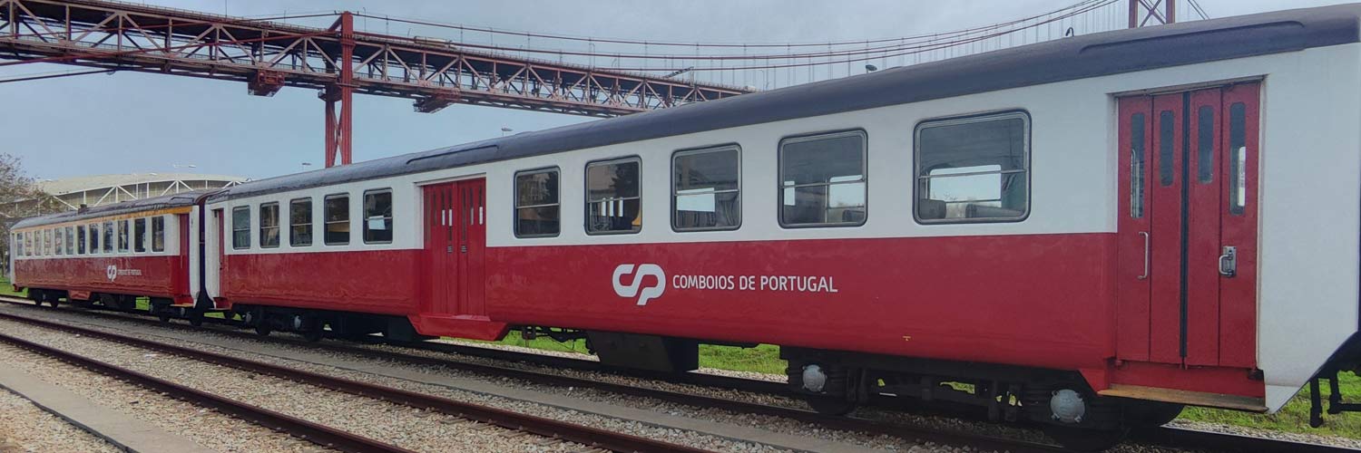 Schindler passenger coaches with red and white livery stopped at one of the rail lines.
