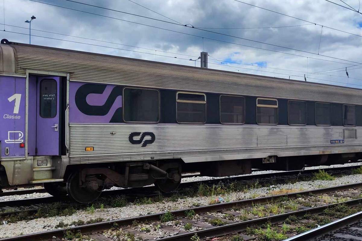 Carruagem Sorefame de 1ª classe cor roxo e cinzento parqueada numa das linhas da estação.