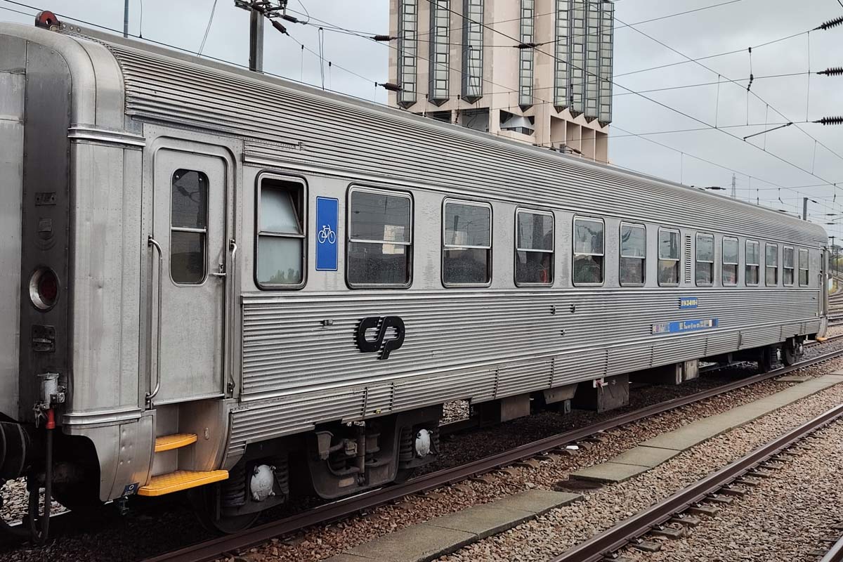 Carruagem Sorefame de 2ª classe cor cinzento parqueada numa das linhas da estação.