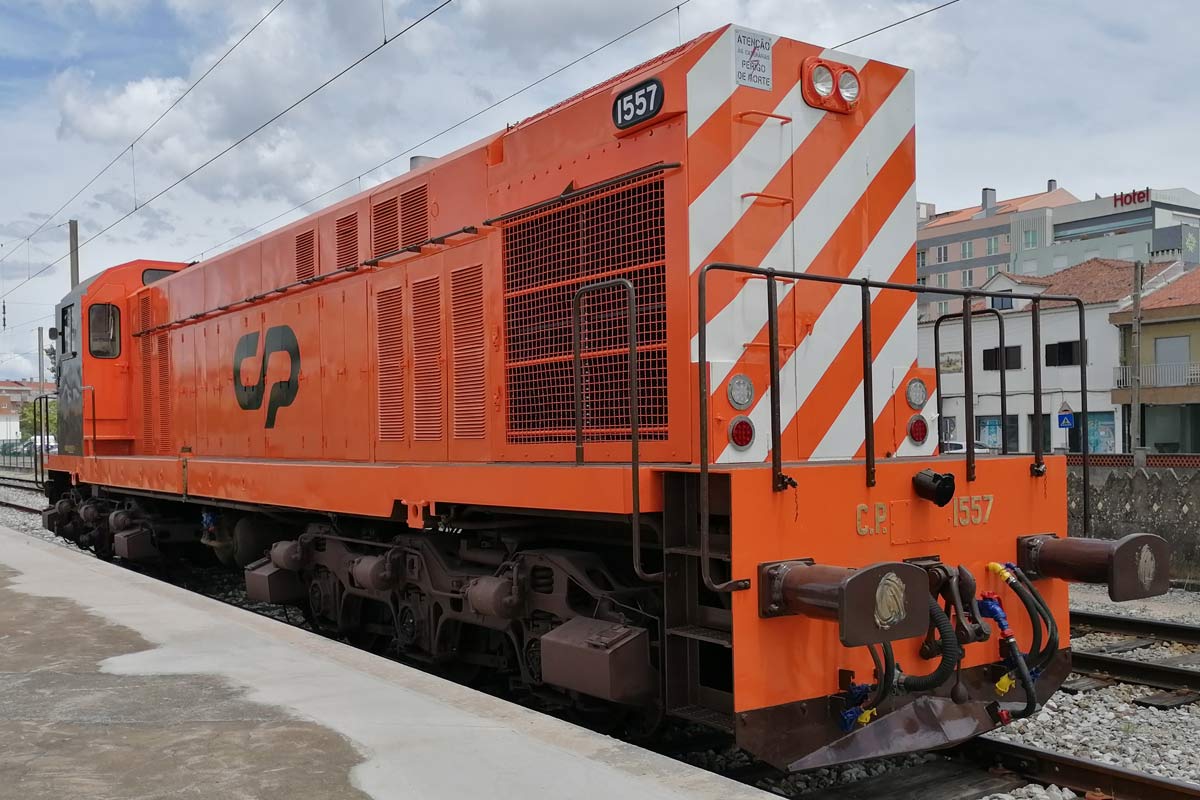 Locomotiva da série CP 1550 cor laranja e com listras brancas na frente, parada numa das linhas da estação.