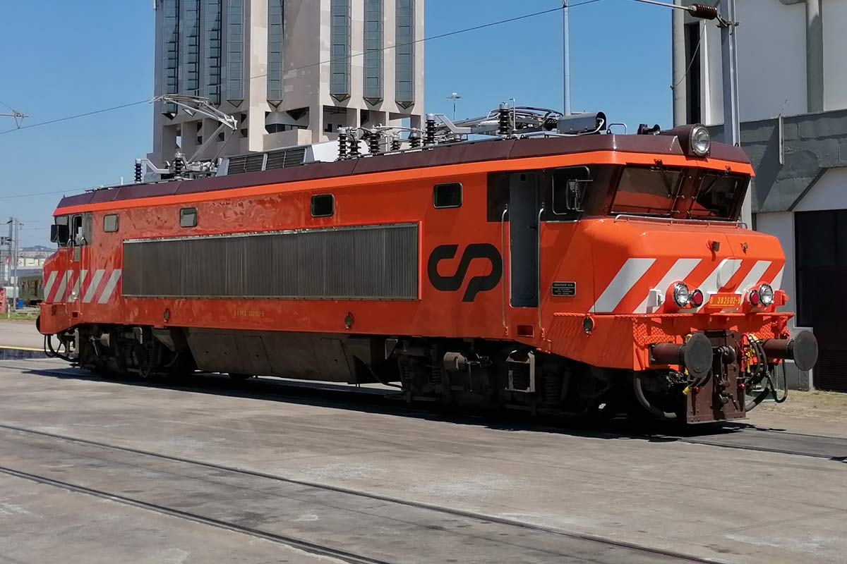 Locomotiva da série CP 2600 cor laranja e com listras brancas na frente, parada numa das linhas da estação.