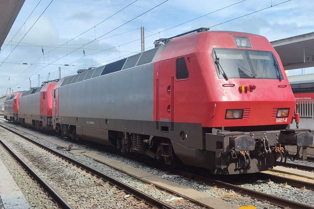 Três locomotivas elétricas da série CP 5600 cor cinza e vermelho, paradas numa das linhas da estação.