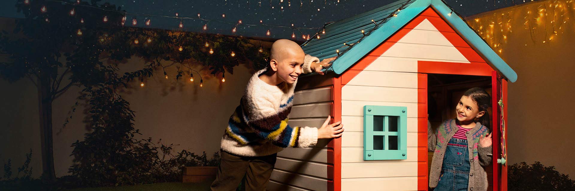 Menino e menina a brincar junto a uma casinha para crianças em cenário de Natal.