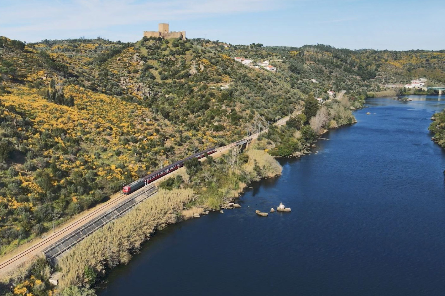 Comboio a passar junto às margens de um rio.