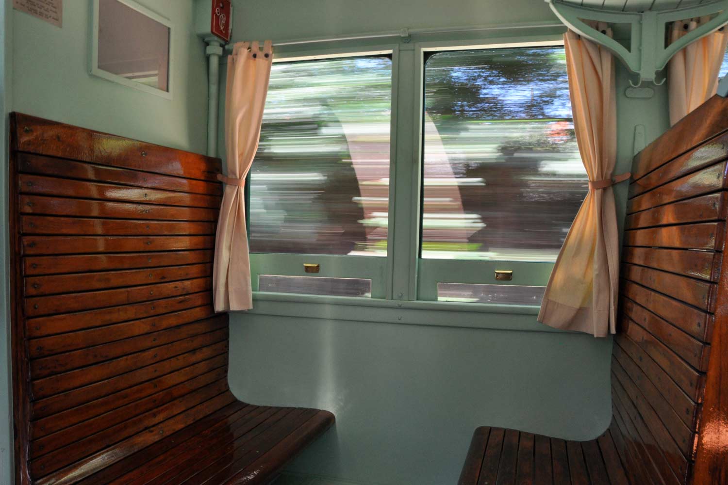 Interior de uma carruagem em movimento, com bancos em madeira e janelas com cortinas.