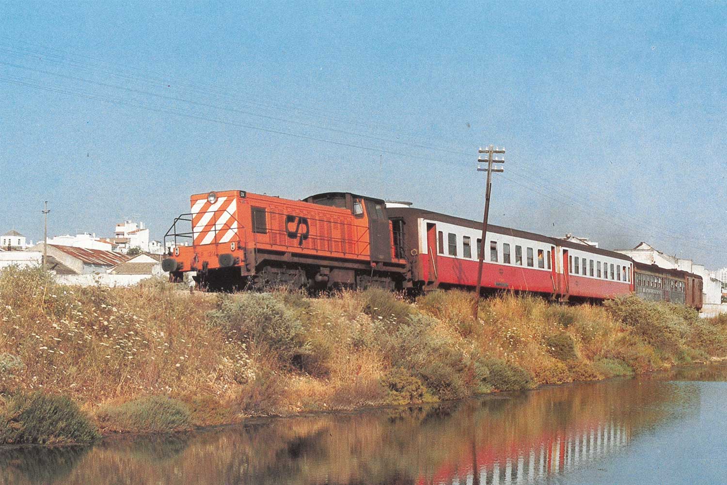 Locomotiva diesel da série CP 1200 com duas carruagens vermelho e branco, uma carruagem cinzenta e um furgão vermelho.