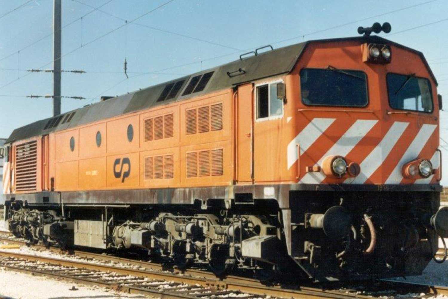 Locomotiva diesel CP 1960 em tons de laranja, castanho e branco, parada numa das linhas da estação.