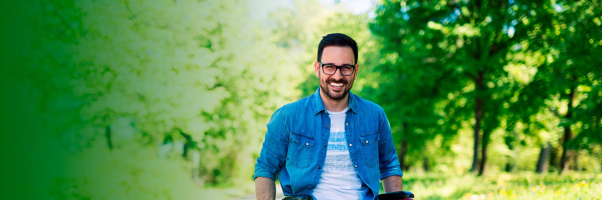Homem sorridente em cadeira de rodas, com árvores e vegetação ao fundo.