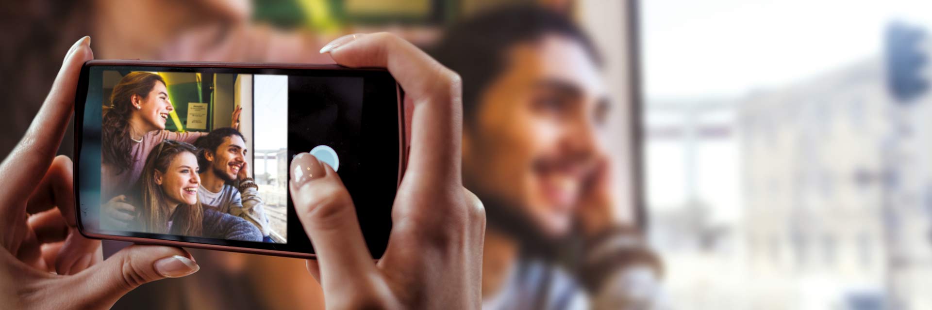 Mãos de mulher a tirar foto com telemóvel a 3 jovens junto à janela de comboio.