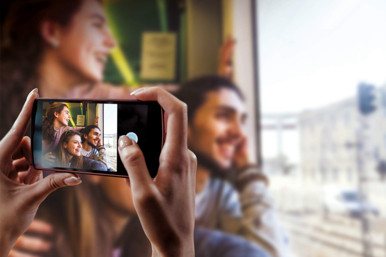 Mãos de mulher a tirar foto com telemóvel a 3 jovens junto à janela de comboio.