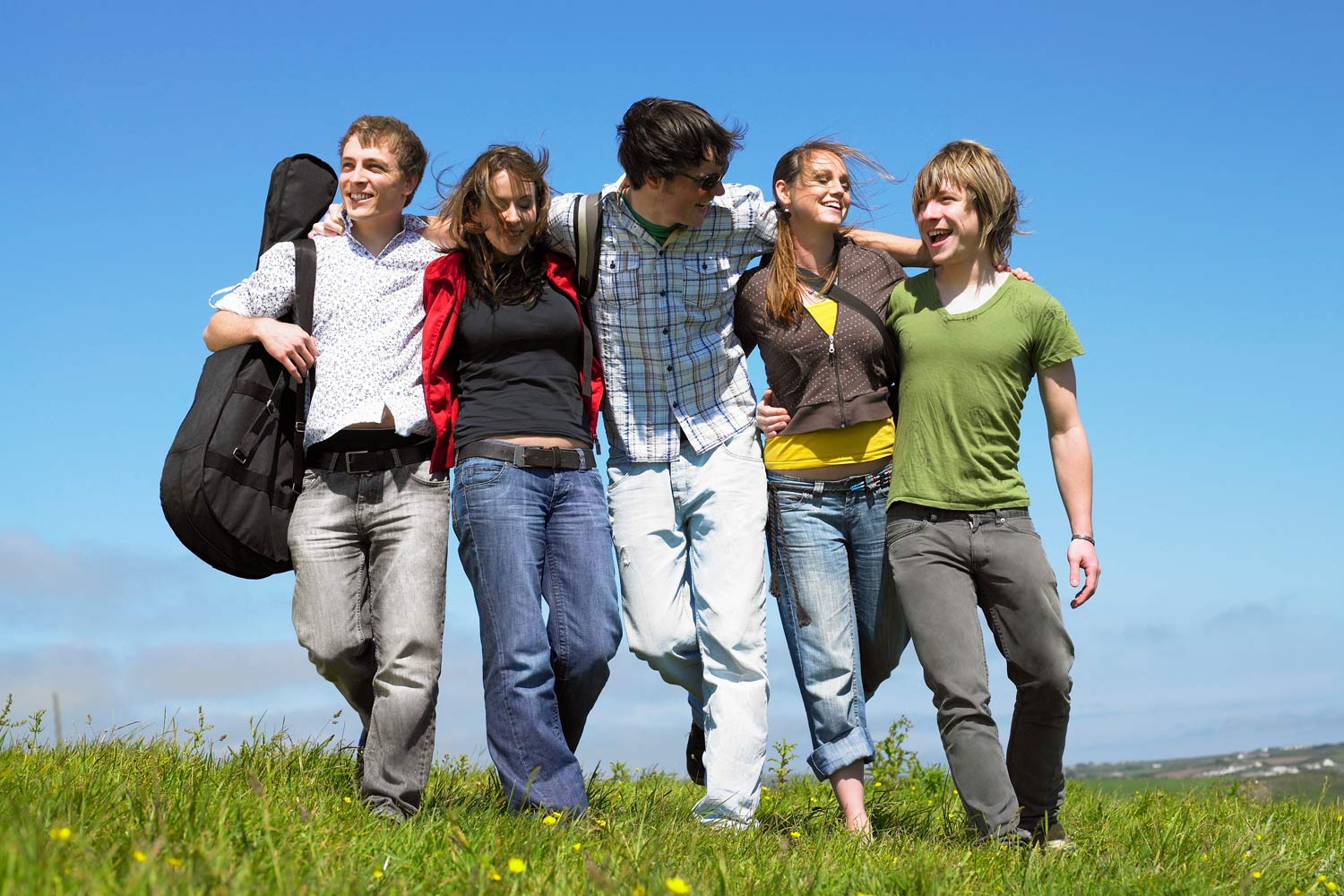 Cinco jovens abraçados, com céu azul atrás.
      