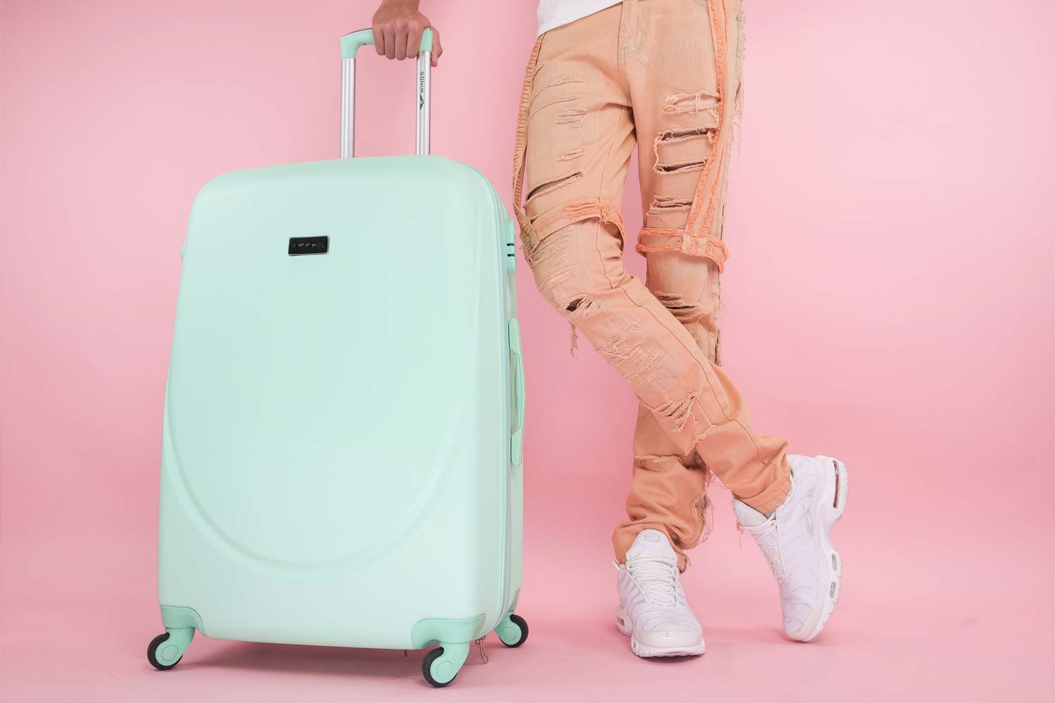 Pés de Cliente e trolley de viagem ao lado, sobre um fundo rosa.