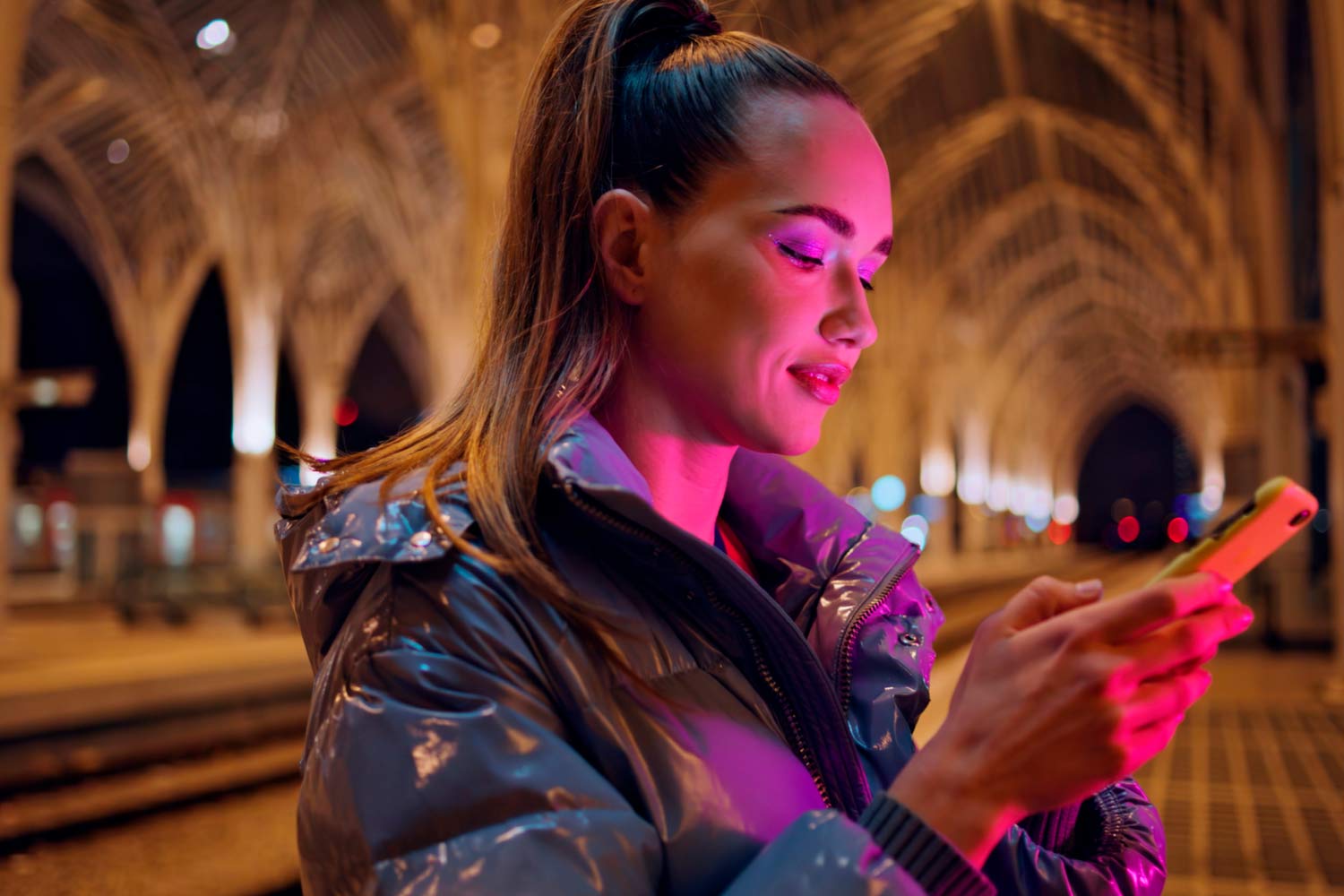 Mulher a consultar  um smartphone, à noite, na plataforma da estação do Oriente.