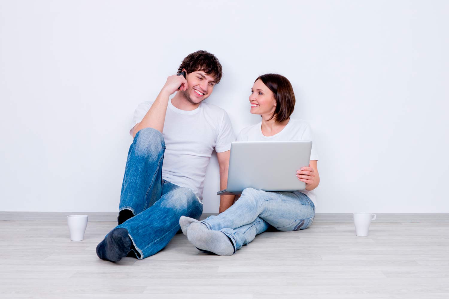 Rapaz sentado no chão ao telemóvel junto de rapariga ao portátil.