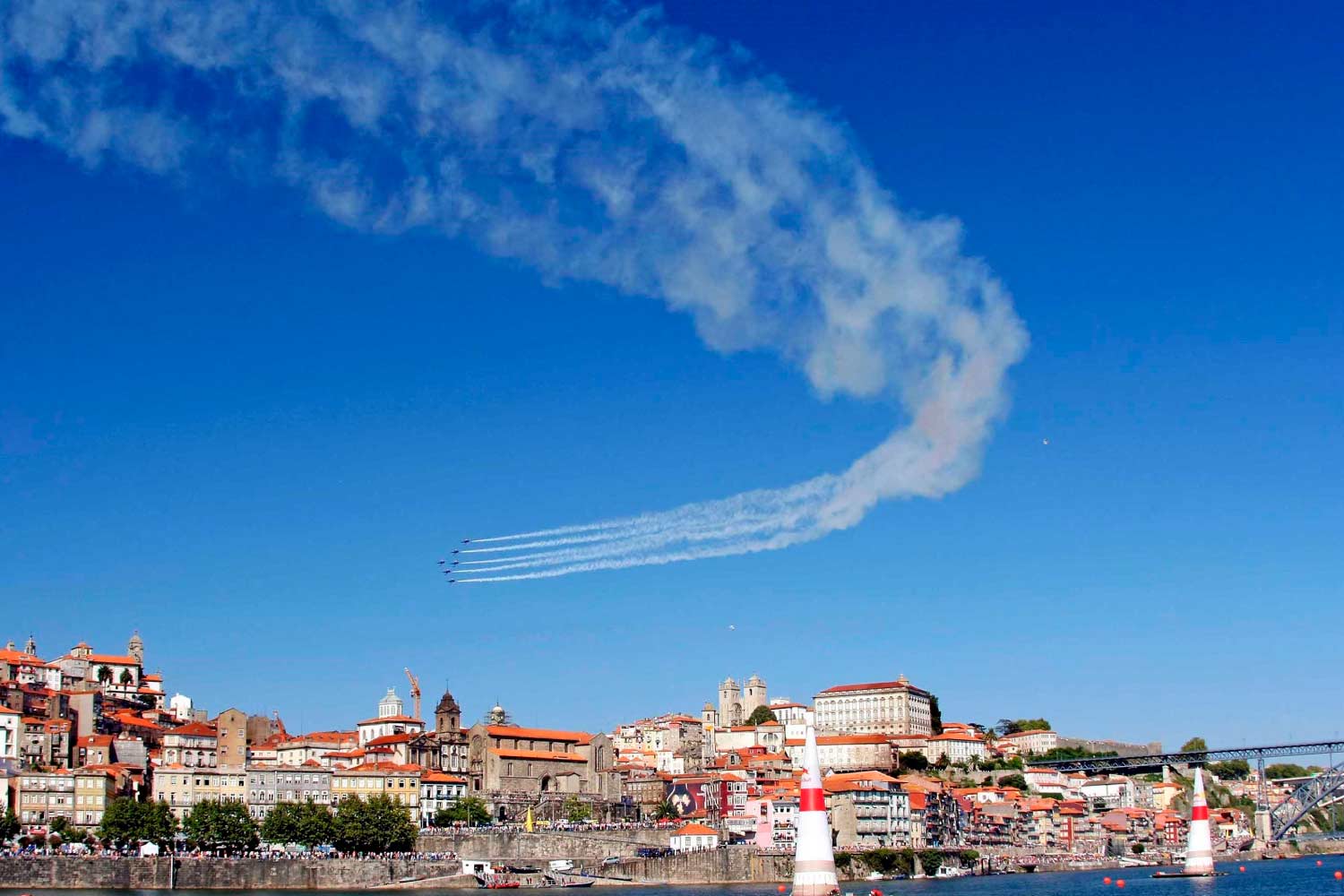 Aviões em formação exibindo fumos brancos em céu azul, sobre a Cidade do Porto, com vista do rio e da Ribeira.
