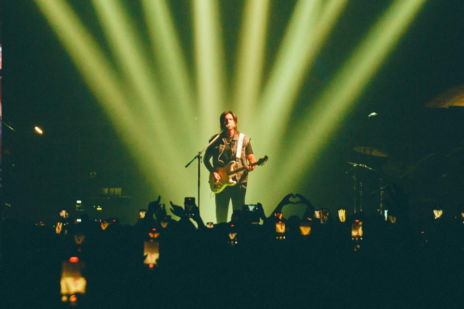 Juanes em palco com foco de luzes, com os fãs a gravar o concerto todos com os telemóveis levantados