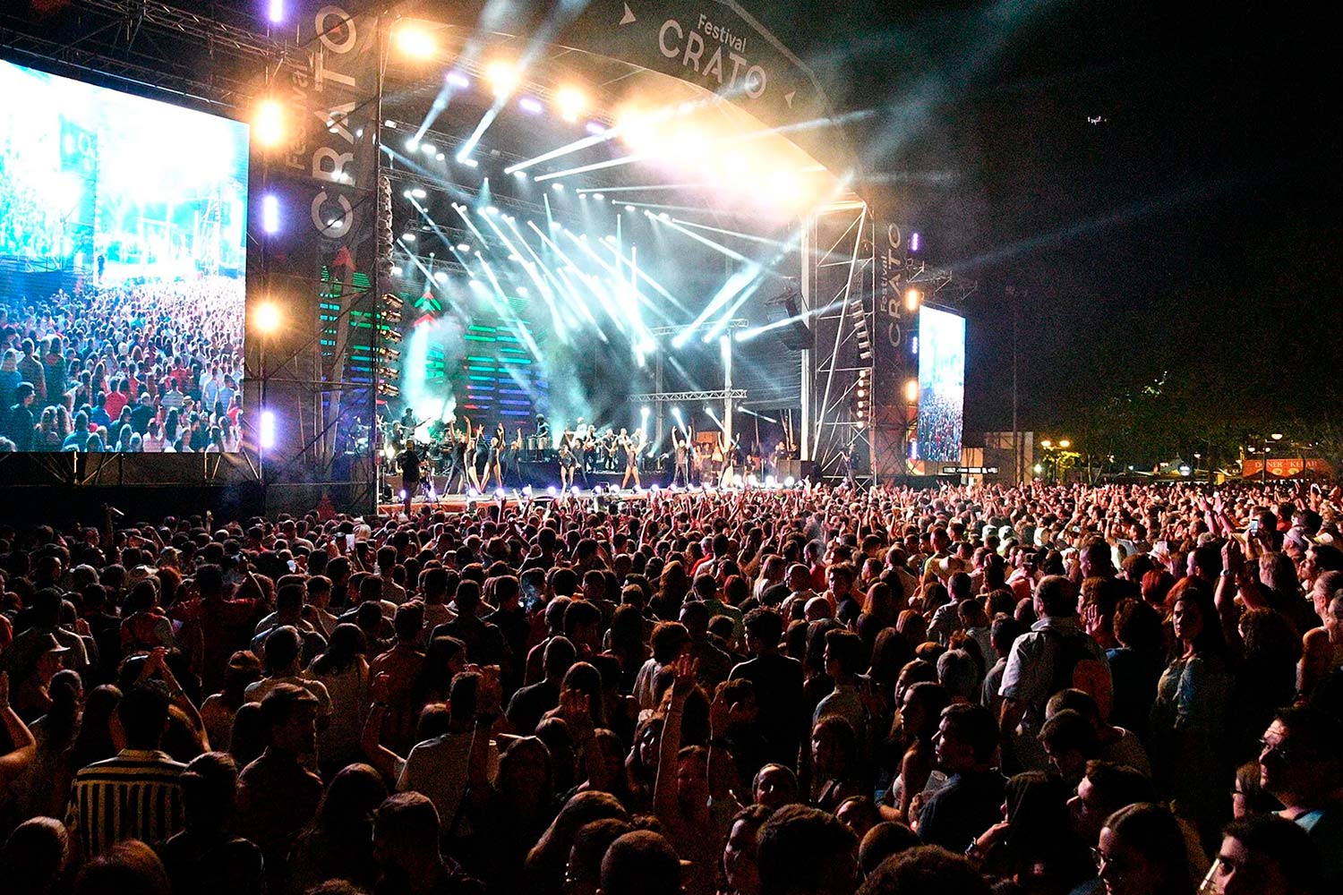 Imagem a cores noturna de pessoas a assistir concerto de música.