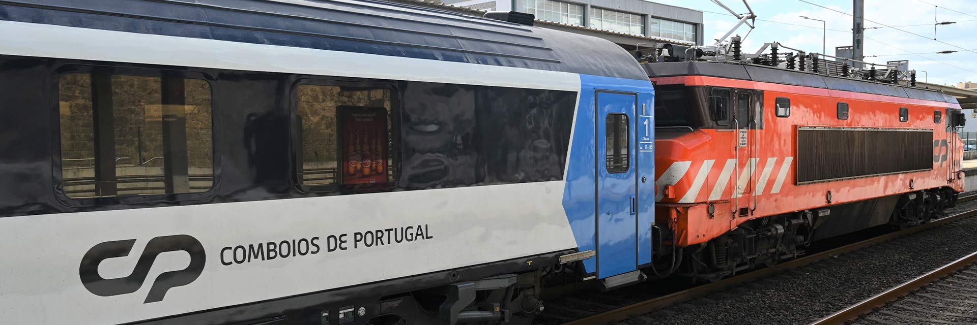 Imagem a cores de carruagem Arco cor branco, azul e preto, e de locomotiva elétrica da série CP 2600, cor laranja, branco e castanho escuro.