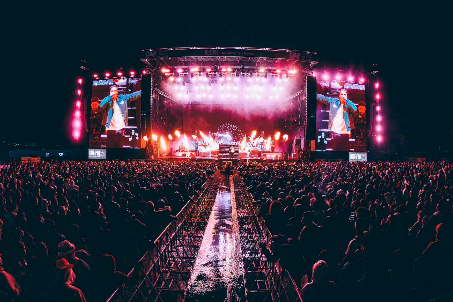 A night-time shot of a stage with a band performing and people watching the concert.