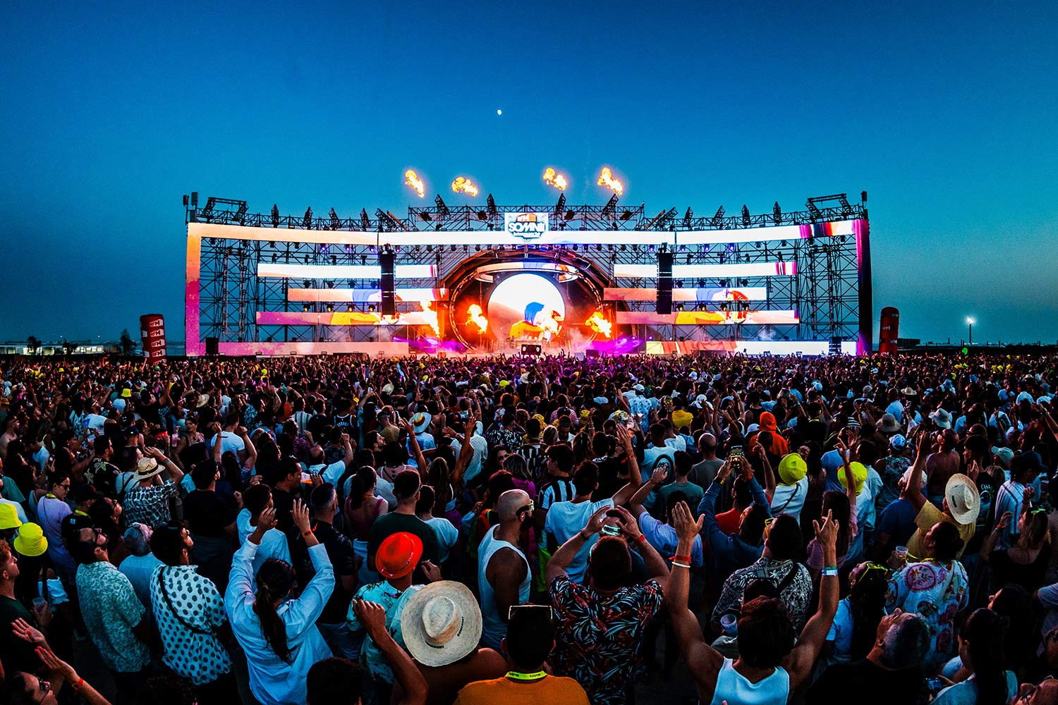 Imagem noturna de pessoas junto a palco, com dj a atuar.