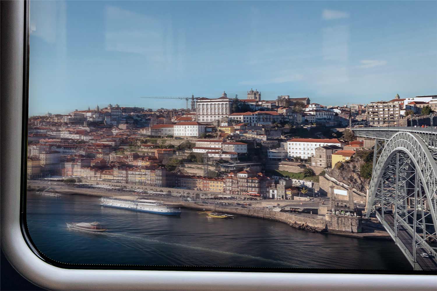 Pela janela do comboio, a vista da ribeira do Porto onde se ve o Rio Douro com barcos, o casario e a ponte Dom Luís.